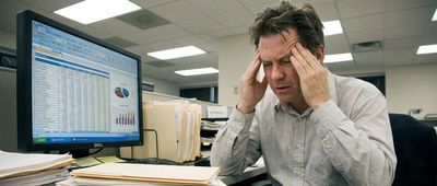 Ein frustrierter Büroangestellter vor einem Bildschirm voller komplexer Excel-Tabellen